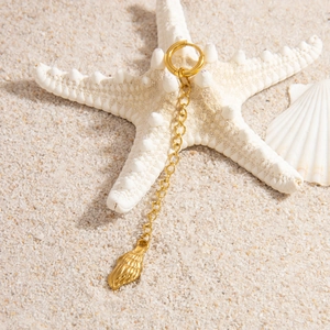 Close-up of a 18K gold shell pendant earring with a long chain on white sand