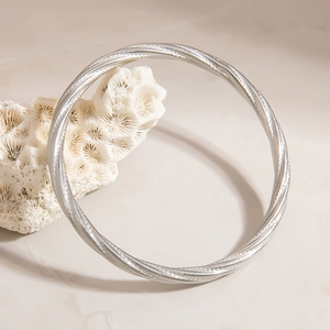 Macro detail of silver twisted cable bracelet hanging on a white coral stone base