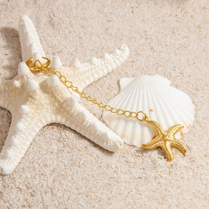 Detailed view of 18K gold starfish pendant on white beach sand with seashells