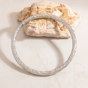 Close-up of silver stainless steel bangle with hammered texture on a natural stone base