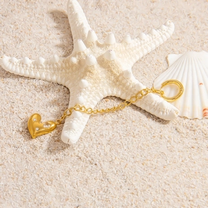 Detail of 18K gold heart pendant with small stones on beach sand with a starfish