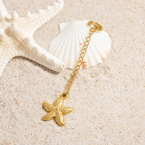 Detailed close-up of 18K gold-plated starfish pendant with buckle on beach sand