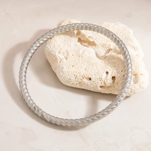 Detail of silver twisted stainless steel bangle with spiral texture on white coral