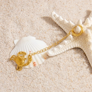 Golden crab pendant accessory displayed on white sand with seashells for ocean jewelry