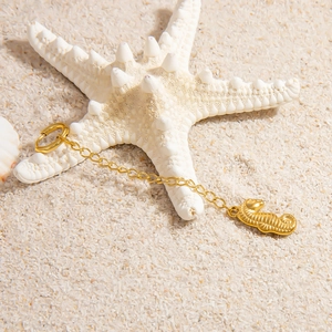 Detail of a 18K gold seahorse pendant on a starfish with a beach sand background