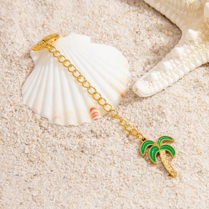 Macro detail of tropical coconut tree gold pendant on sand with starfish and shells