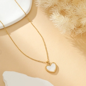 Detailopname van een hartvormige parelmoer hanger met gouden kralenrand aan een fijne ketting