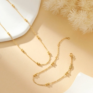 Detail of gold beaded chain necklace with lobster clasp and metal tag on beige stone