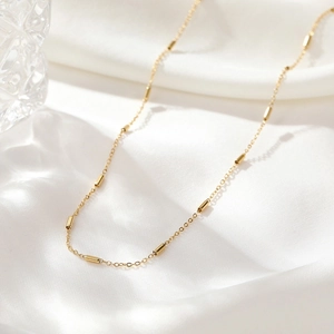 Elegant gold station necklace with cylindrical beads on a fine chain over silk background