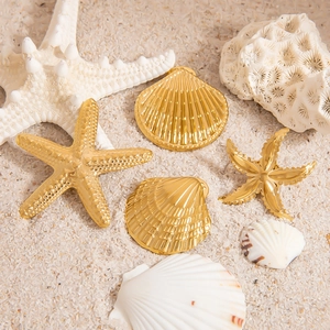 Golden starfish and shell brooches in 18K gold finish on a beach sand background