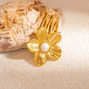 Détail d'un peigne à cheveux doré à fleurs texturées et une perle blanche centrale