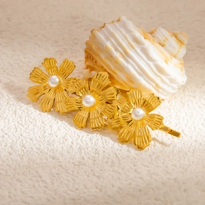 Détail d'une barrette fleurie dorée avec pétales texturés et perles sur fond de coquillage