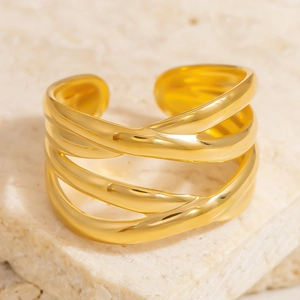 Nahaufnahme eines goldenen, mehrlagigen Cross-Over-Rings auf einem hellen Steingrund