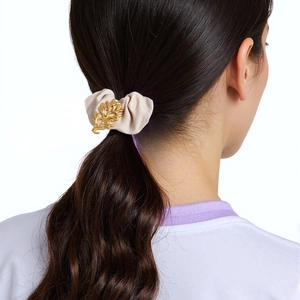 Detail von beigem Satin-Haargummi mit goldenem Korallen-Accessoire am Haar getragen