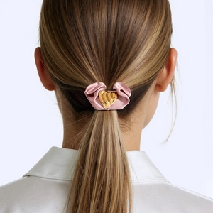 Detail eines rosa Satin-Haargummis mit goldenem Herz-Anhänger am Pferdeschwanz