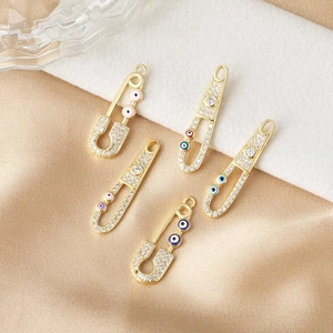 Colgantes de imperdible bañados en oro de 18K con circonitas y dijes de ojo turco