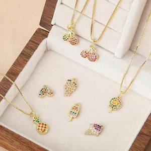 Collane dorate con ciondoli a forma di frutta e caramelle con zirconi su velluto beige