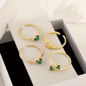 Lot de quatre bagues ajustables dorées avec zircons vert émeraude dans un écrin à bijoux