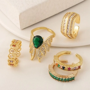 Set of four gold-plated adjustable rings with colored zircons on white marble background