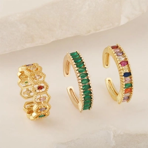 Three gold adjustable rings with colorful marquise zircons on textured stone background