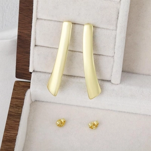 Elegante goldene gebogene Stabohrringe auf einer dunklen Schmuckschatulle aus Holz