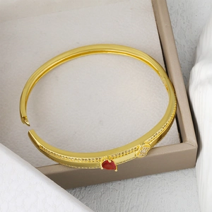 Elegant gold bangle with a red heart-shaped gemstone and sparkling zircon accents