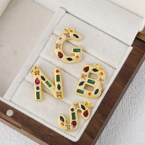 Golden micro-paved letter pendants G, N, B, S with colorful zircon stones in a jewelry box