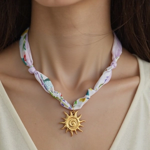 Dettaglio della collana foulard in seta con ciondolo a sole dorato su modella