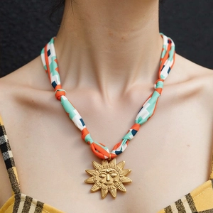 Dettaglio del ciondolo a sole dorato su una collana in sciarpa di seta colorata