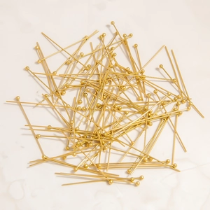 Close-up of golden ball head pins for jewelry making on marble surface
