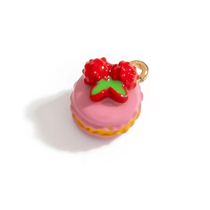 Dettaglio di ciondolo macaron rosa con fragola rossa e anello in metallo dorato