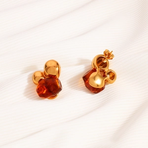 Macro detail of Mickey-shaped gold metal and amber resin earrings on soft fabric