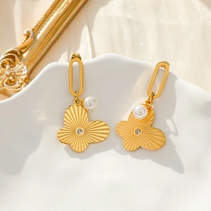 Detailansicht goldener Schmetterlings-Ohrringe mit Perlen auf weißem Dekoteller