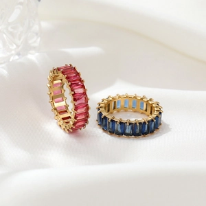 Elegant gold eternity rings with red and blue baguette-cut zircons on white silk background