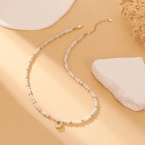 Close-up of white beaded necklace with oval zircon pendant and heart-shaped tag