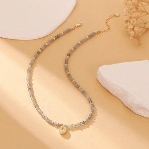 Detail of beaded gemstone necklace with faceted grey beads and a gold zircon pendant