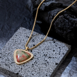 Collier avec pendentif Unakite triangulaire et chaîne dorée sur fond de pierre volcanique