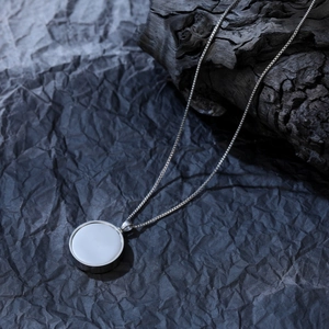 Dettaglio della collana urna in argento con intarsio bianco su sfondo di legno rustico