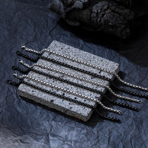 Détail de bracelets à mailles noires et argentées sur une surface en pierre texturée