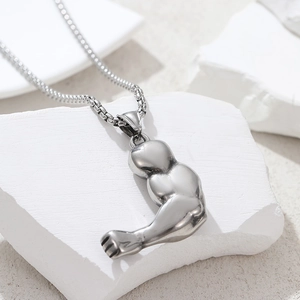 Polished silver muscle arm pendant on pearl chain displayed on white stone slab