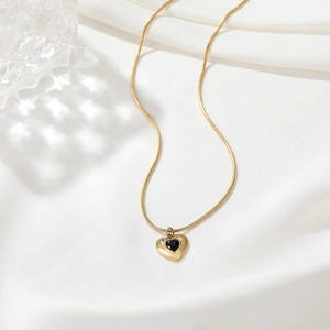 Detail einer goldenen Schlangenkette mit einem Herzanhänger und schwarzem Edelstein