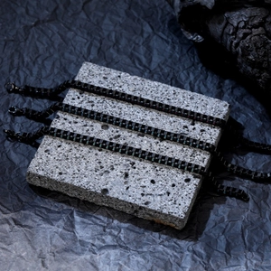 Trois bracelets gourmette noirs en acier inoxydable sur roche volcanique au style industriel