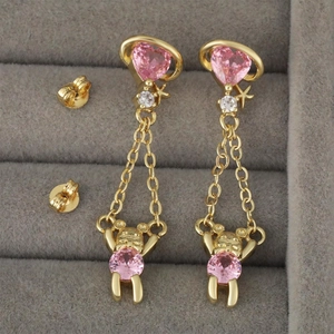 Goldene Ohrhänger mit rosa Herz-Edelsteinen und kleinen Bären auf grauem Samttablett