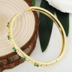 Elegant gold bangle with green emerald gemstones and white enamel floral details