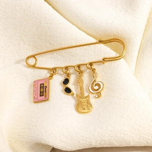 Detailed view of gold safety pin brooch with guitar, cassette, and music note charms