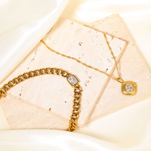 Elegante gouden set met vierkante zirkoon ketting en armband op beige steen