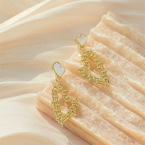 Elegant gold heart earrings with white enamel inlay on silk and marble background