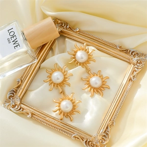 Elegant gold sun-shaped pearl drop earrings displayed on silk inside a vintage frame