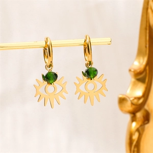 Détail de boucles d'oreilles œil porte-bonheur dorées avec perles vertes sur support