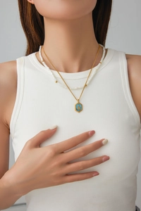 Detail of gold snake pendant on blue hex charm layered with white beaded necklace